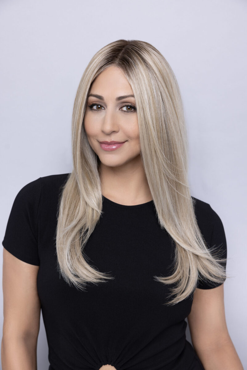 Woman with straight, long blonde hair wearing a black short-sleeve top, posing against a plain light background.